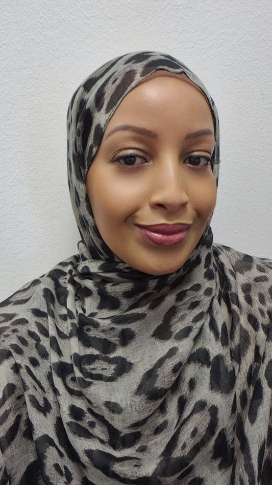 A woman wearing the Stylish Cheetah Hijab by Bihi Boutique smiles softly at the camera, posed against a plain white wall.