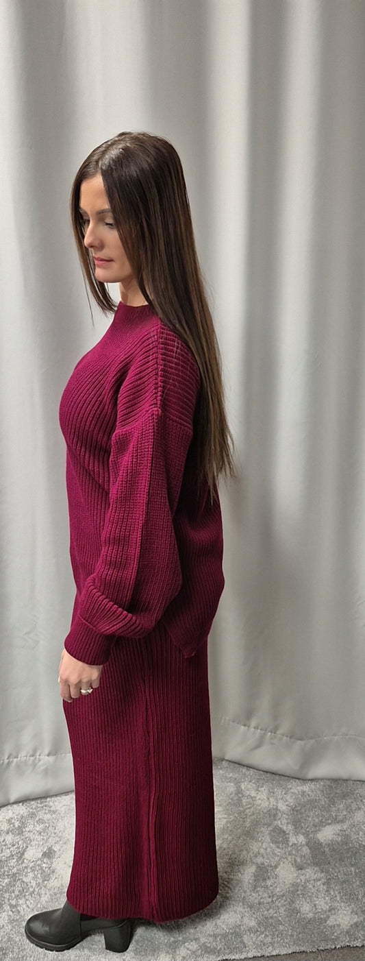 A woman with long straight brown hair stands sideways in front of a light gray curtain, wearing the Bihi Boutique Cozy Burgundy Sweater & Skirt Set (One Size, Wool Blend) paired with black ankle boots.