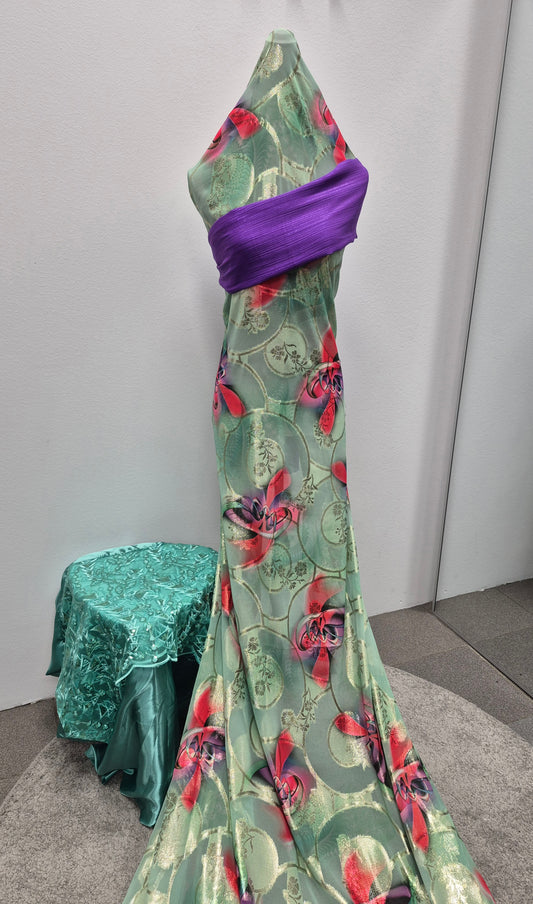 A mannequin showcases the Bihi Boutique Shop Fransawi Dirac: Elegant & Stylish Boutique Dress in shiny green and red floral fabric with a bold purple sash. A small round table in matching green sits beside it, all set against a plain white wall.