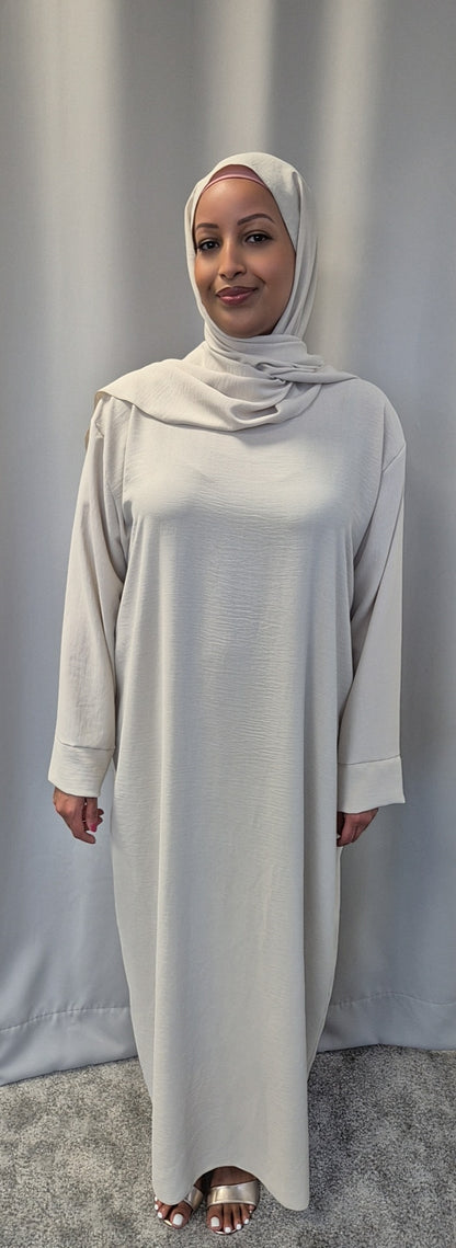 A woman wearing the Elegant Black One Size Prayer Clothing by Bihi Boutique stands on a gray carpet before a plain, light curtain, smiling gently at the camera.