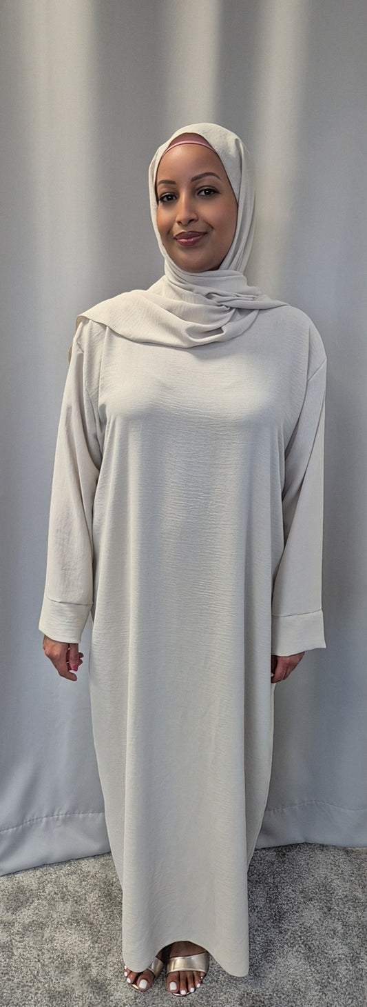A woman wearing the Elegant Black One Size Prayer Clothing by Bihi Boutique stands on a gray carpet before a plain, light curtain, smiling gently at the camera.