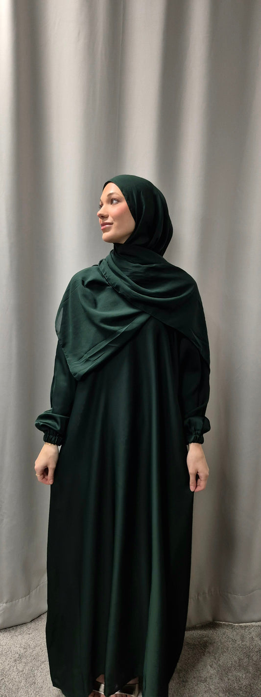 A woman in the Bihi Boutique Amina Abaya with Chiffon Hijab (Size 56) stands before light gray curtains, looking to the side with a calm expression.