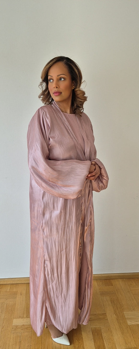 A woman stands on a wooden floor against a white wall, wearing the Elegant Pink Organza Slipdress with Chiffon Hijab from Bihi Boutique and white pointed-toe shoes. She gazes calmly to her left. Shop now!.