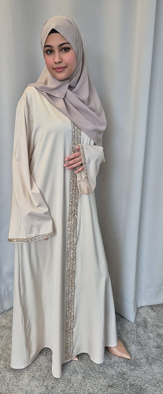 A woman in Bihi Boutiques Aurelia Ivory & Rose Dress—an elegant S/M fashion essential—smiles softly, one hand near her chest and the other by her side, standing before a pale curtain in a light gray hijab.