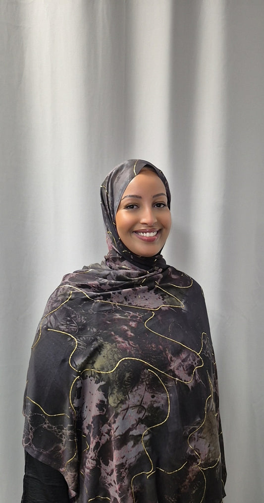 A woman smiles at the camera wearing Bihi Boutiques Elegant Marble Chiffon Hijab—stylish, lightweight, and perfect for any look—paired with dark clothing against a light gray curtain backdrop.