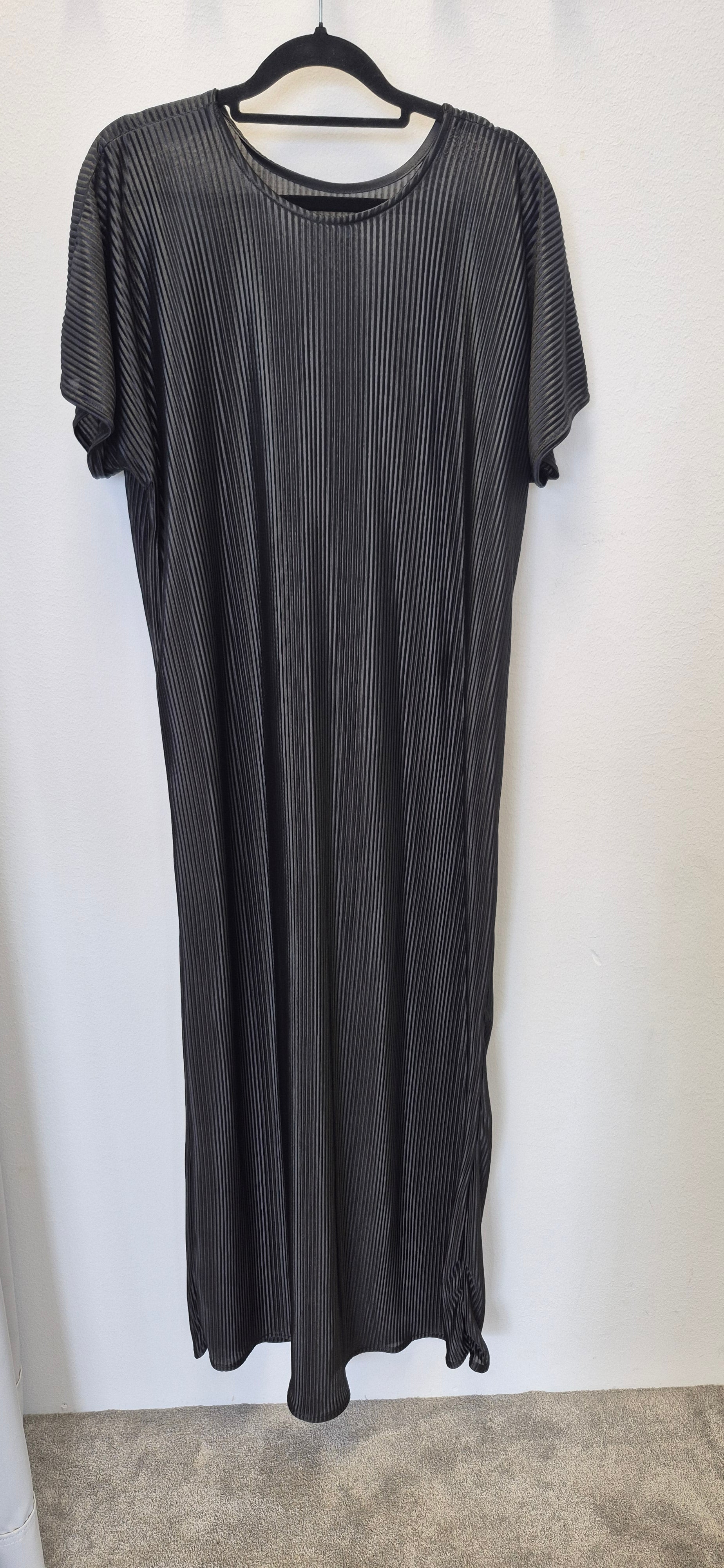 The Chic Black Slip Dress by Bihi Boutique, featuring short sleeves, a loose fit, thin white diagonal stripes, and a subtle bottom knot, hangs on a black hanger against a plain white wall. It falls below the knee—effortless style for any occasion.