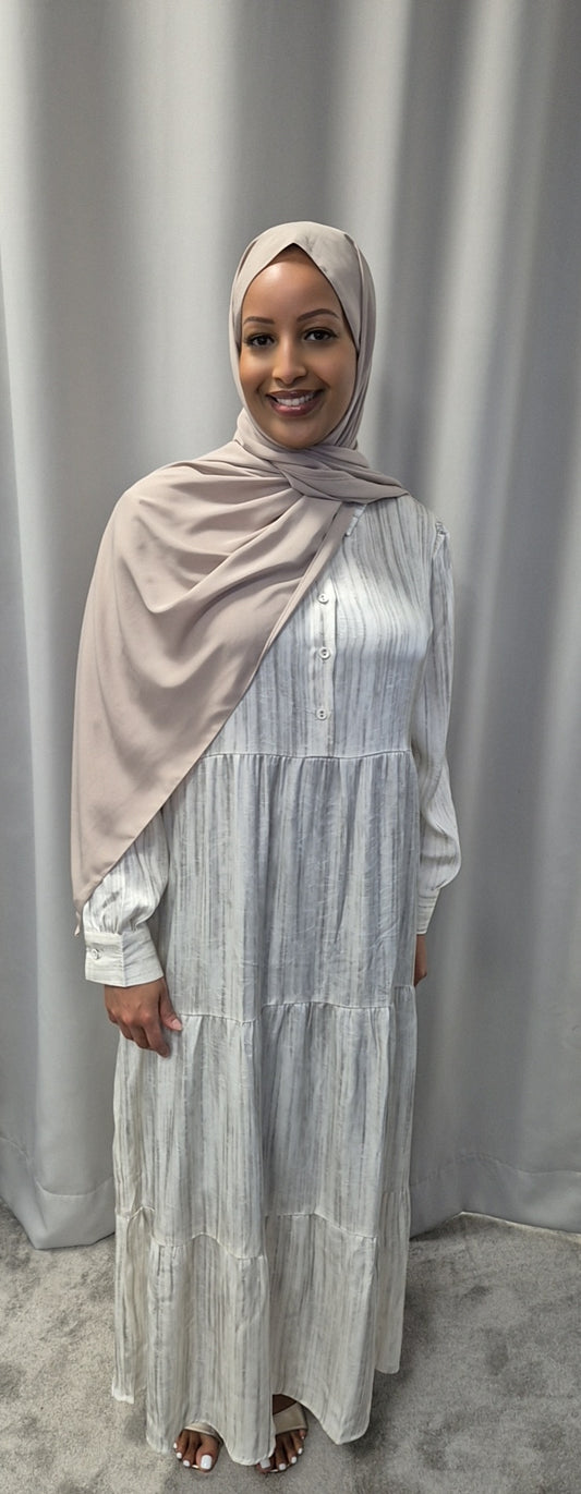 A woman smiles in front of gray curtains, wearing the Shop Celeste Noir & Ivory Satin Dress by Bihi Boutique, available in sizes S/M & L/XL. She stands on a light carpet with her hands by her sides.