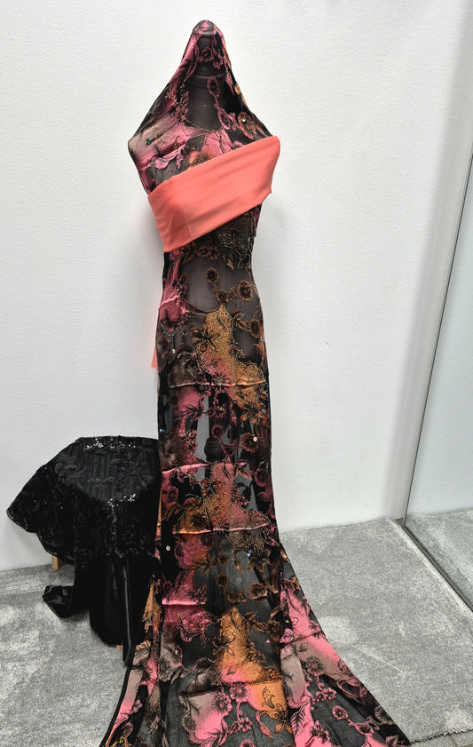 A black dress form displays the Shop Stylish Fransawi Dirac Half Bac Elegant Fashion Piece by Bihi Boutique—an elegant sheer, floor-length gown with pink and orange floral patterns and a coral sash, shown on gray carpet near a mirror and draped black lace.
