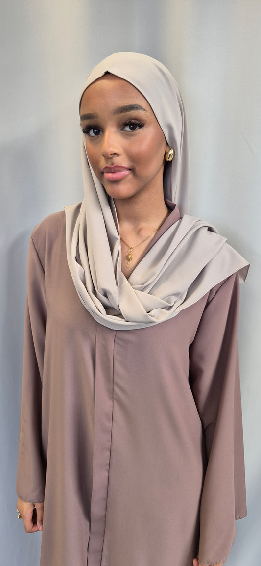 A woman stands against a light gray background, wearing gold earrings and natural makeup, with a Shop Medina Seide Grey-Beige Throw (180x170 cm) from Bihi Boutique draped elegantly over her shoulders.