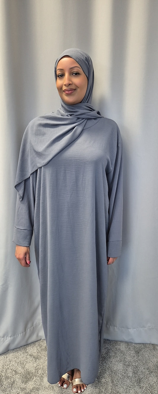 A woman wearing the Elegant Black One Size Prayer Clothing by Bihi Boutique stands on a grey carpet in front of a grey curtain, smiling at the camera.