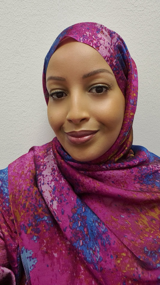 A woman smiles softly at the camera wearing the Bihi Boutique Stylish Printed Chiffon Hijab—an elegant, lightweight hijab in vibrant pink, purple, and blue—set against a plain white background.