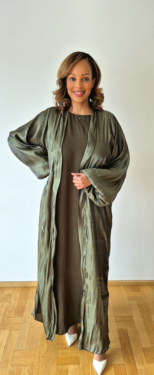 A woman stands indoors on a wooden floor, wearing the Shop Stylish Organza Zaytun Slipdress & Chiffon Hijab (Size 58) by Bihi Boutique, with her hair in loose waves and a neutral background behind her.