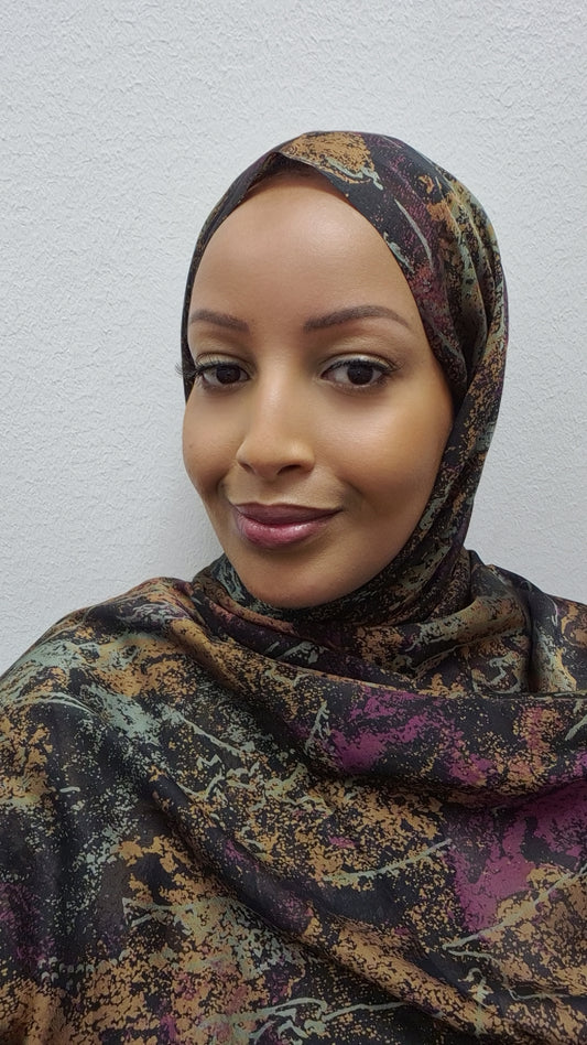 A woman wearing the Lightweight Chiffon Hijab from Bihi Boutique smiles gently while standing in front of a white textured wall, showcasing this stylish and versatile accessory.