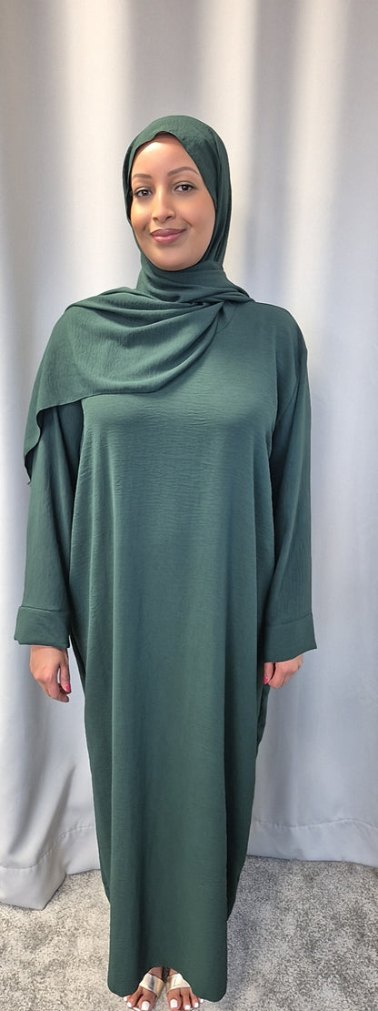 A woman stands in front of a light grey curtain, wearing the Elegant Black One Size Prayer Clothing by Bihi Boutique, suitable for all sizes. She smiles gently with her hands relaxed at her sides.