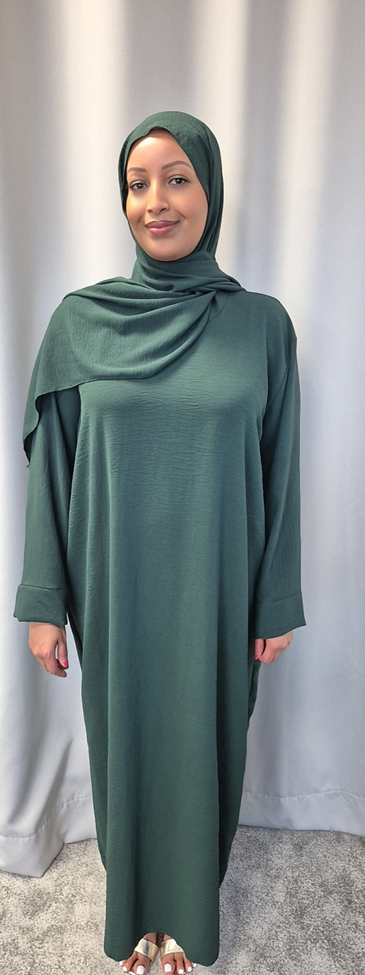 A woman stands in front of a light grey curtain, wearing the Elegant Black One Size Prayer Clothing by Bihi Boutique, suitable for all sizes. She smiles gently with her hands relaxed at her sides.