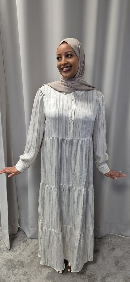 A smiling woman in the Celestial Ivory Satin Dress (Size S/M) by Bihi Boutique stands before a grey curtain, her arms relaxed at her sides, showcasing an elegant and chic look.