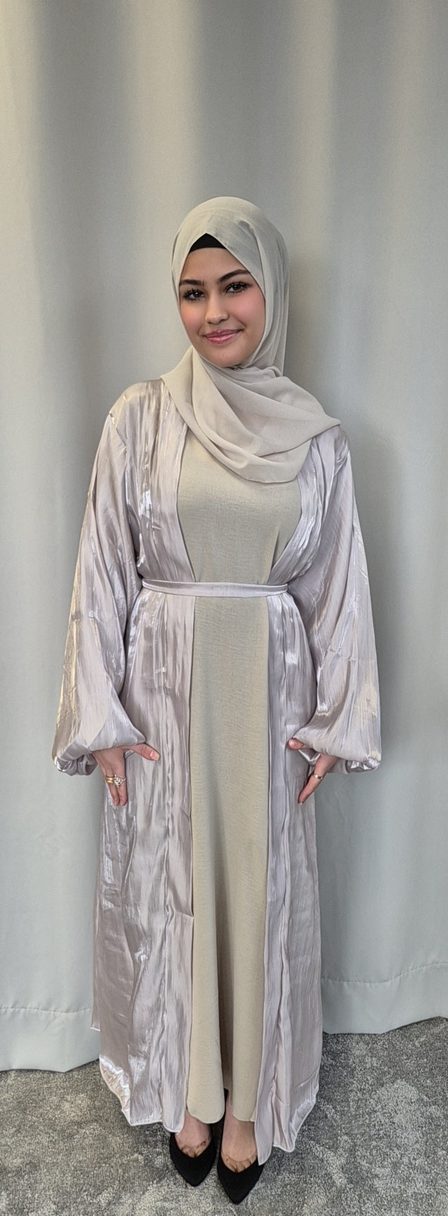 A woman smiles gently at the camera, wearing the Bihi Boutique Stylish Organza Chrome Hijab Set—a chic, lightweight fashion ensemble—in front of a plain light curtain.