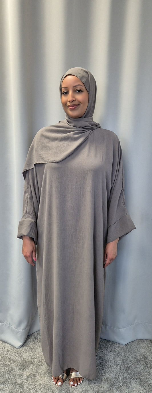A woman wearing the Elegant Black One Size Prayer Clothing from Bihi Boutique stands in front of light gray curtains, smiling gently with her hands by her sides.
