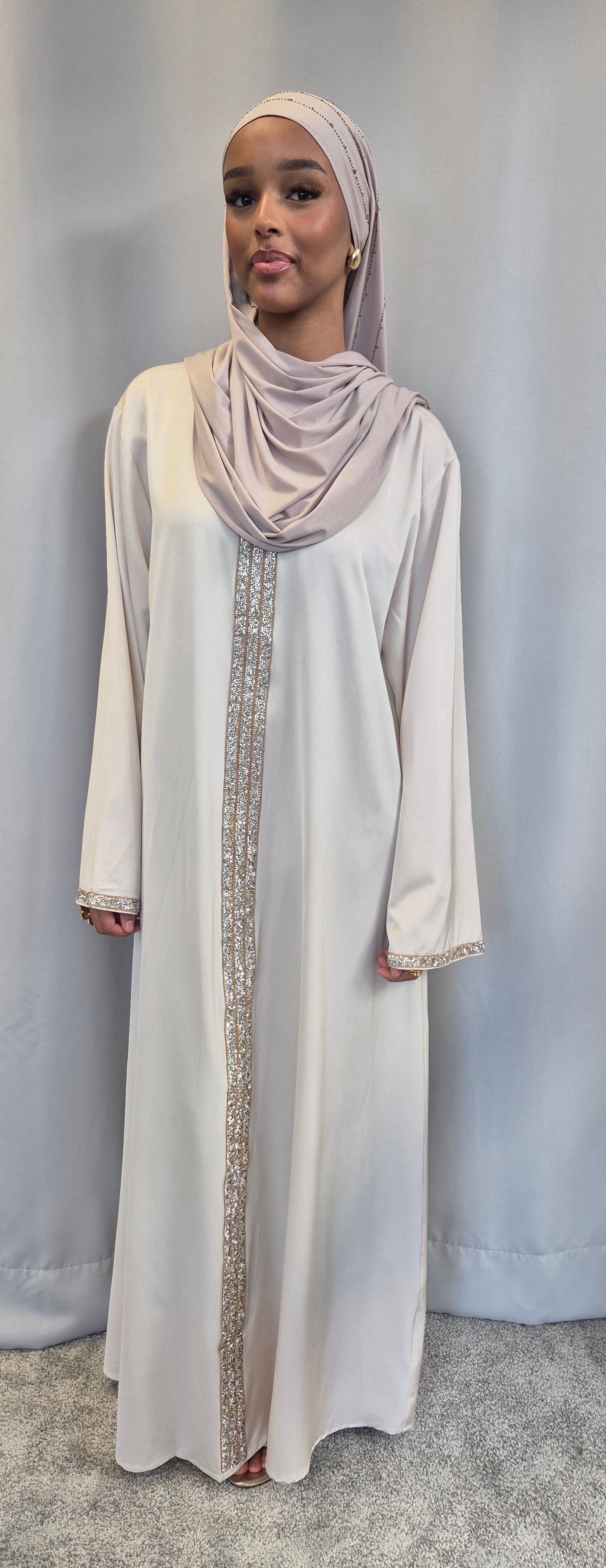 A woman wearing the Aurelia Ivory & Rose Dress by Bihi Boutique, featuring gold embroidery and a matching hijab, stands against a light gray background.