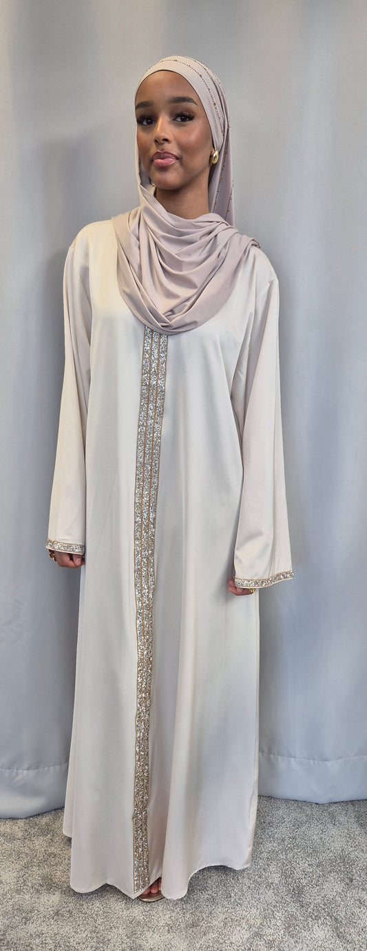 A woman wearing the Aurelia Ivory & Rose Dress by Bihi Boutique, featuring gold embroidery and a matching hijab, stands against a light gray background.
