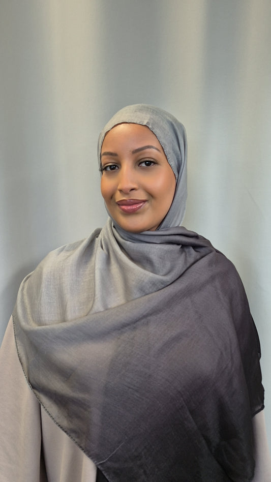 A woman in a Bihi Boutique Ombre Hijab—crafted from stylish cotton and viscose—smiles softly while wearing a light top against a plain background.